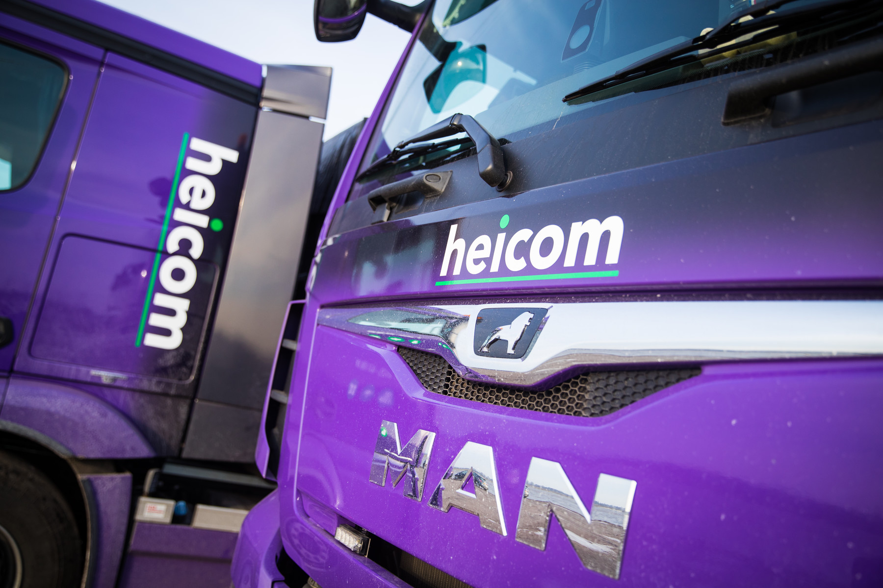 Voorkant van twee paarse MAN-vrachtwagens met het heicom-logo
