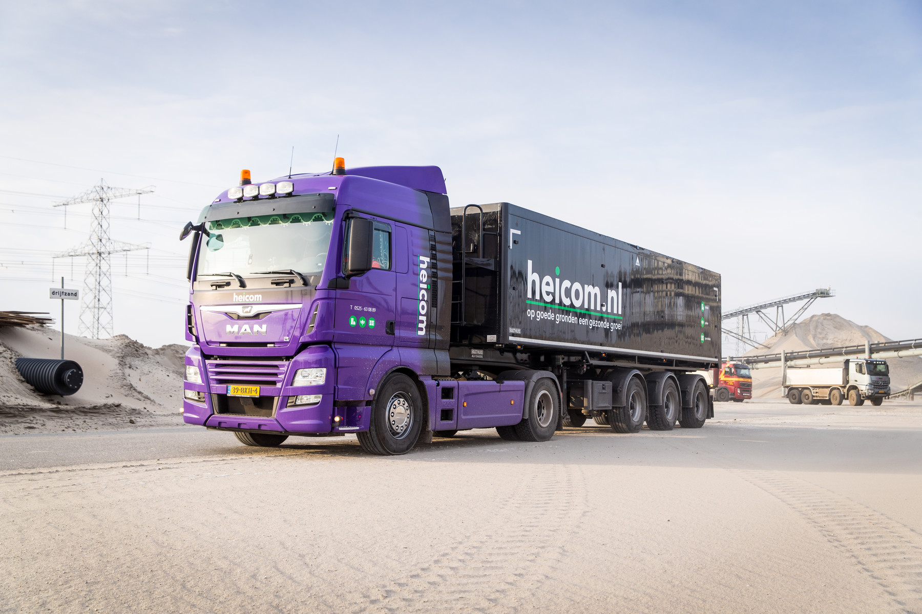 Paarse Heicom-vrachtwagen met kiepoplegger op een zandopslagterrein