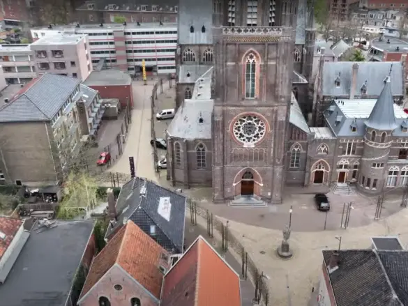 Luchtfoto van een kaal kerkplein met bestrating en geparkeerde auto's
