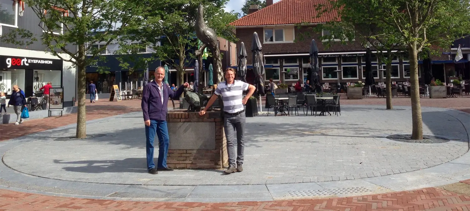 Twee mannen bij een gemetselde zuil op een winkelplein met terrassen