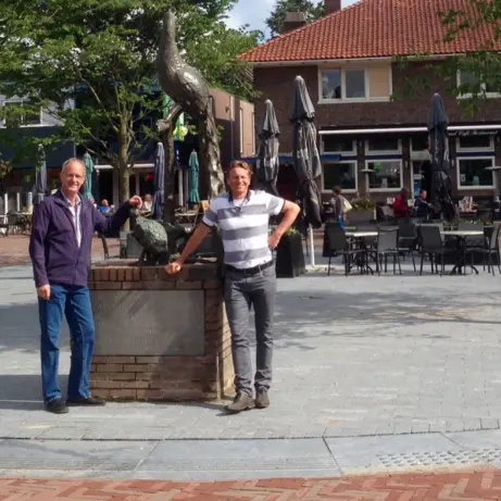 Twee mannen bij een gemetselde zuil op een winkelplein met terrassen