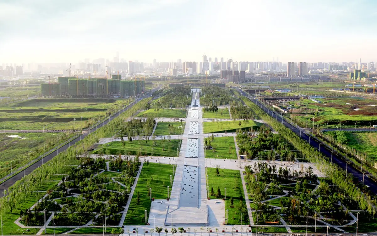 Luchtfoto van een groot stadspark met brede promenade en skyline erachter
