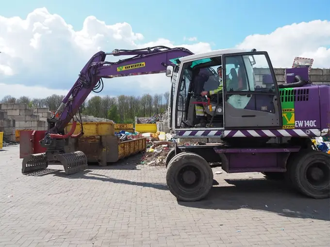 Paarse mobiele kraan met sorteergrijper bij afvalcontainers op een verhard terrein