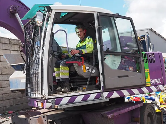 Jongeman in veiligheidsvest in de cabine van een paarse mobiele kraan