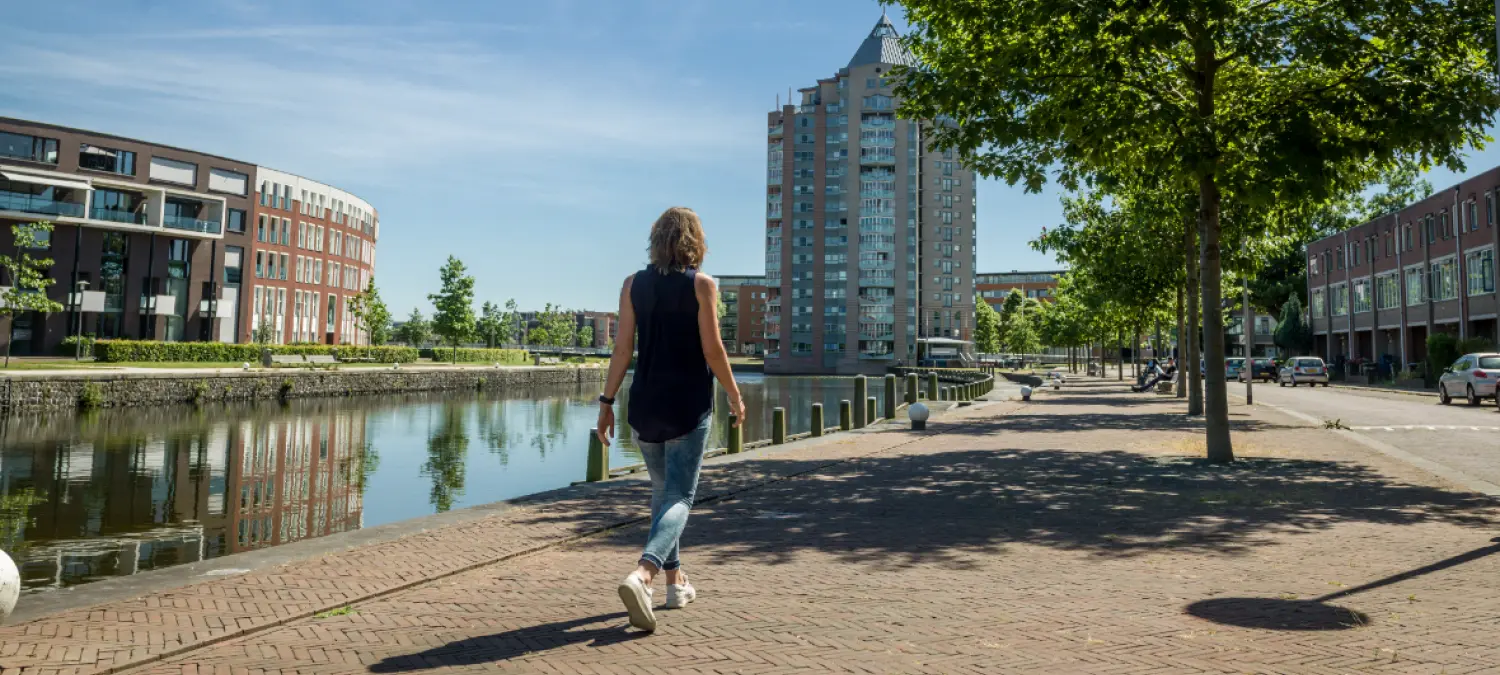 Vrouw wandelt over een bakstenen kade langs een kanaal met flats