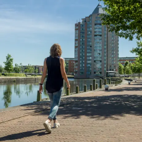 Vrouw wandelt over een bakstenen kade langs een kanaal met flats