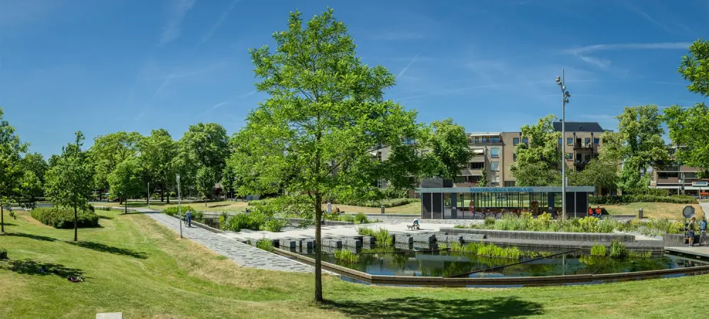 Park met wadi en waterpartij, gazons en bomen onder een blauwe lucht