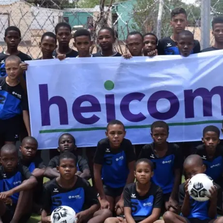 Groep kinderen in voetbaltenue houdt een Heicom-spandoek vast