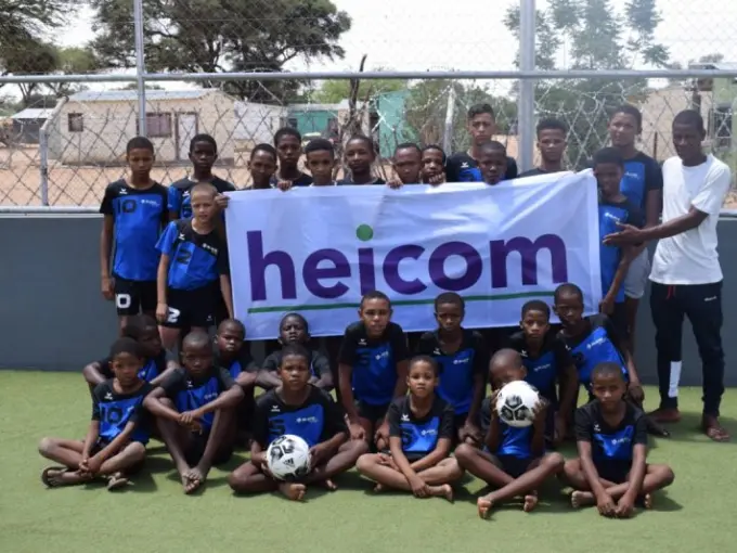 Groep jongens in blauwe voetbalshirts houdt een heicom-spandoek omhoog