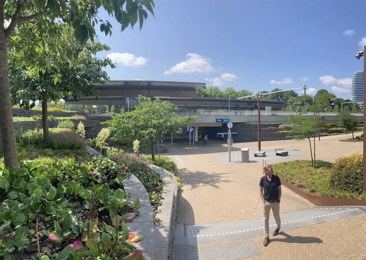 Man op een stationsplein met beplante taluds en jonge bomen