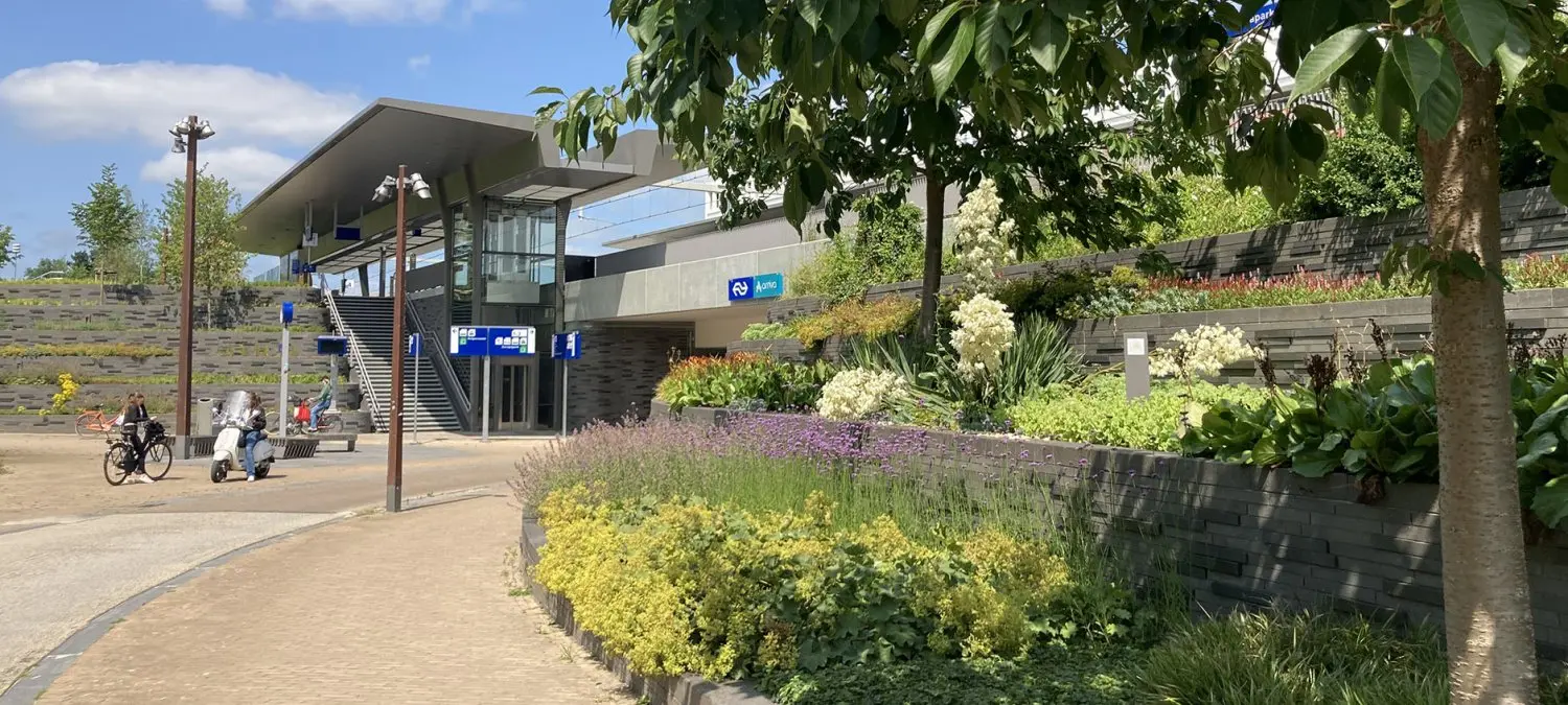 Bloemborders en keermuren voor een stationsgebouw met fietsers op het plein