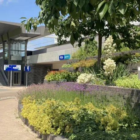 Bloemborders en keermuren voor een stationsgebouw met fietsers op het plein