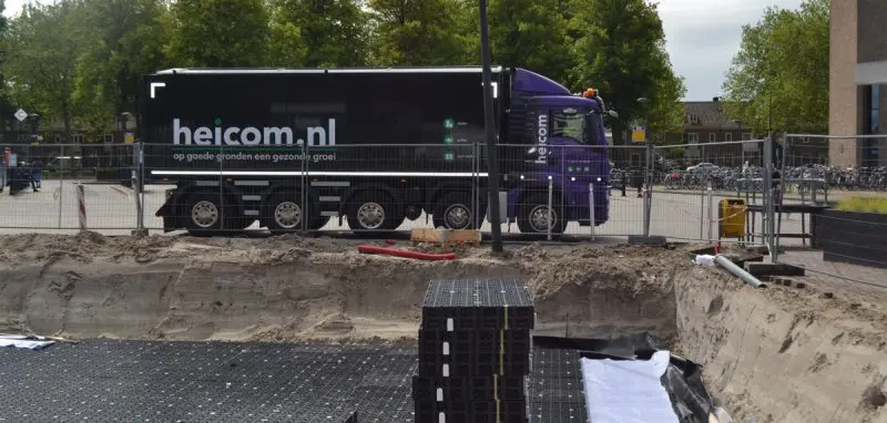 Vrachtwagen van Heicom bij een bouwput met zwarte waterbergingskratten