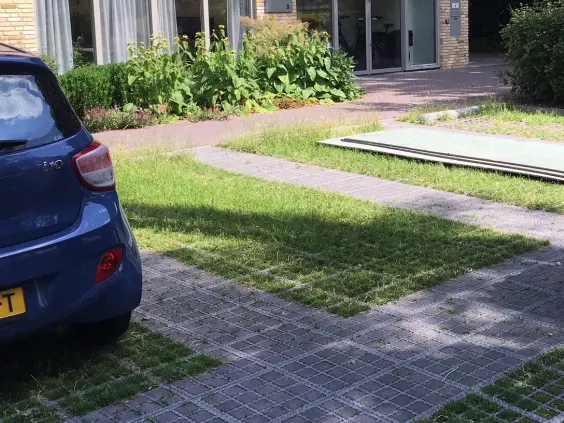 Blauwe auto geparkeerd op grasklinkers voor een kantoorgebouw