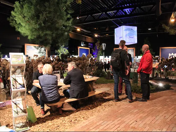 Beursbezoekers aan een picknicktafel tussen bomen en boomschors