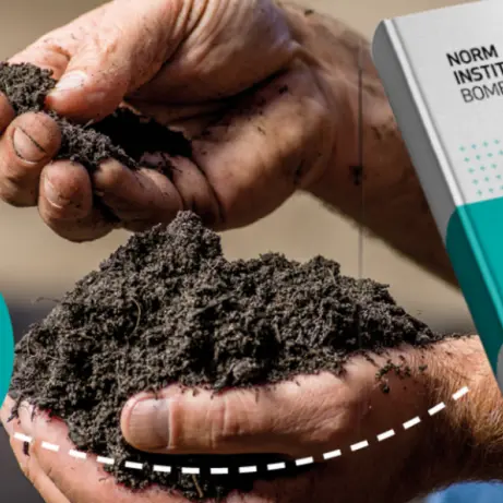 Handen met donkere grond naast het boek Handboek Bomen
