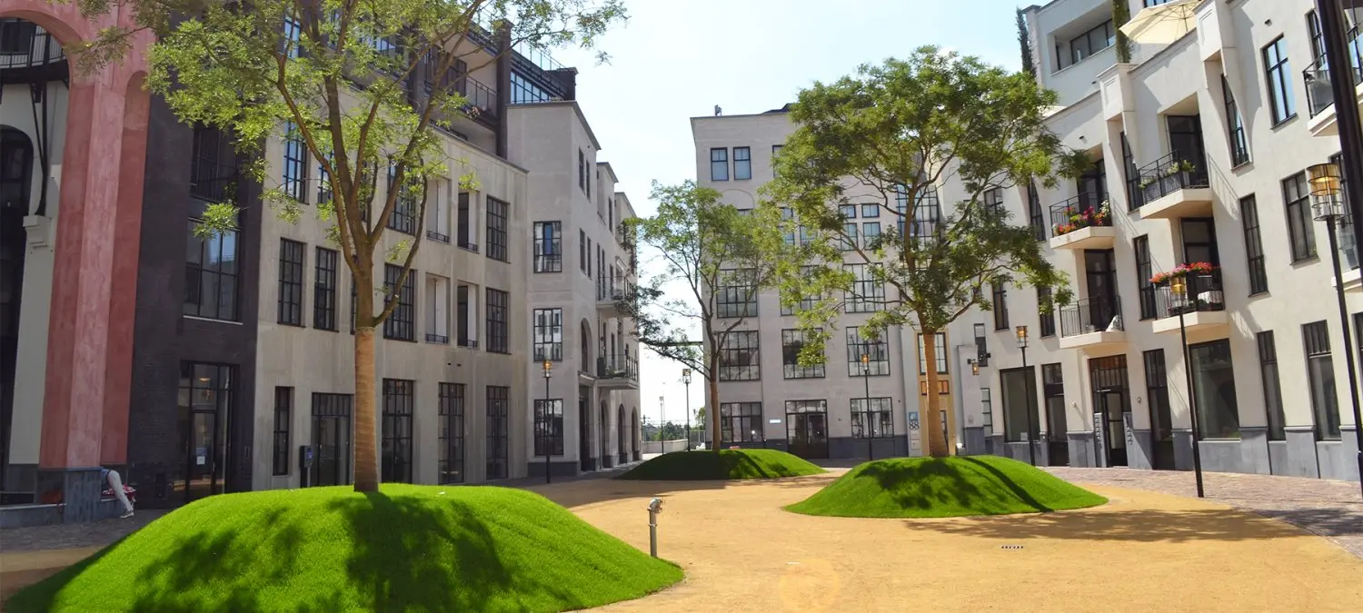 Binnenhof met grasheuvels en jonge bomen tussen appartementengebouwen