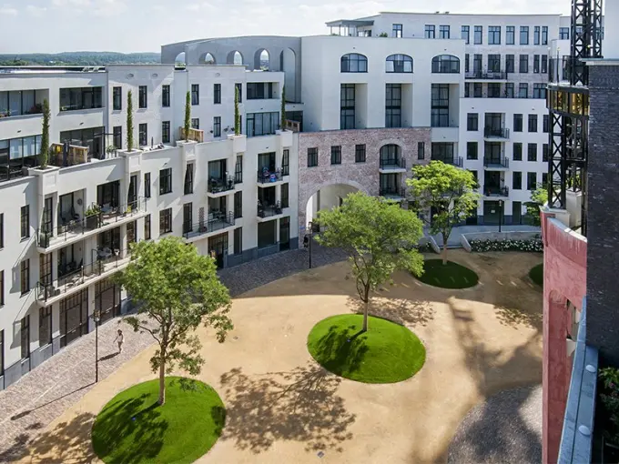 Binnenhof met bomen op ronde grasheuvels tussen witte appartementen