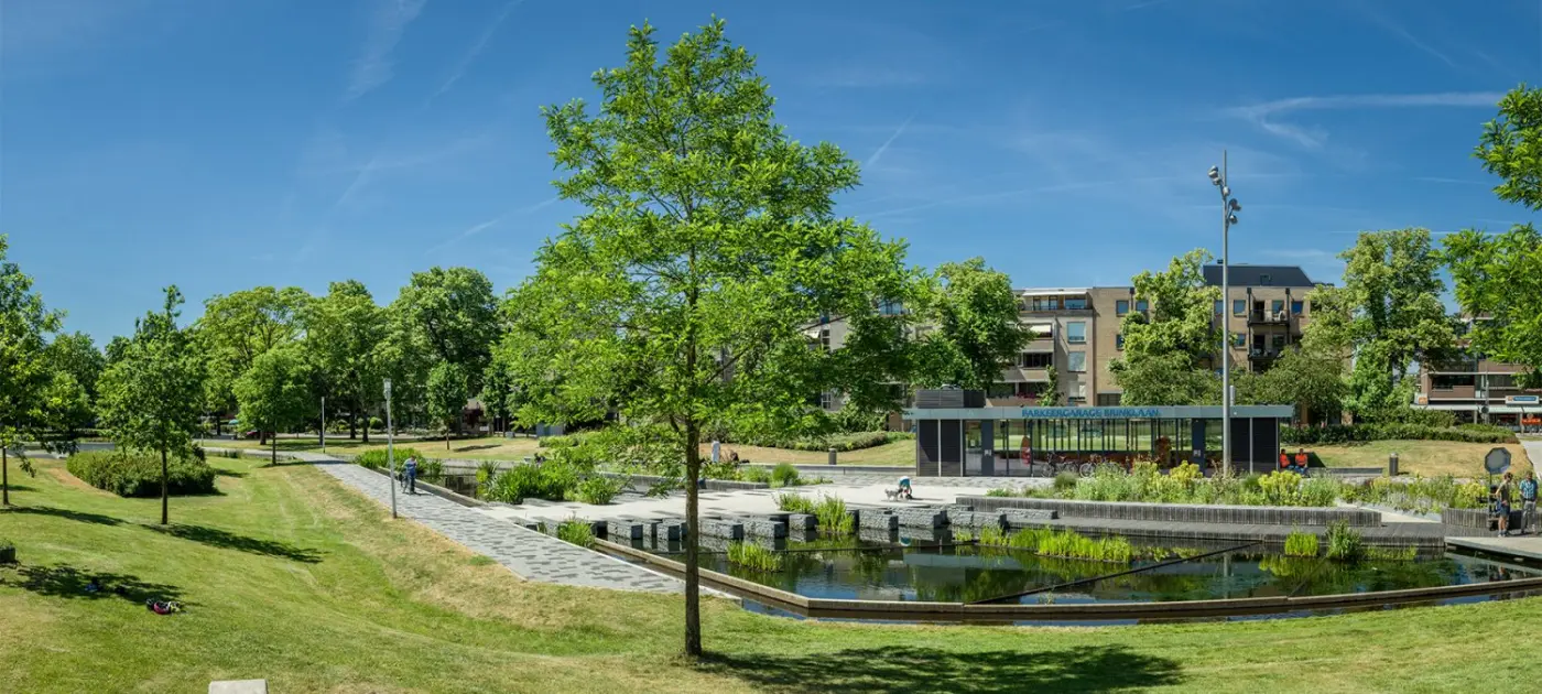 Park met wadi en waterpartij, gazons en bomen onder een blauwe lucht