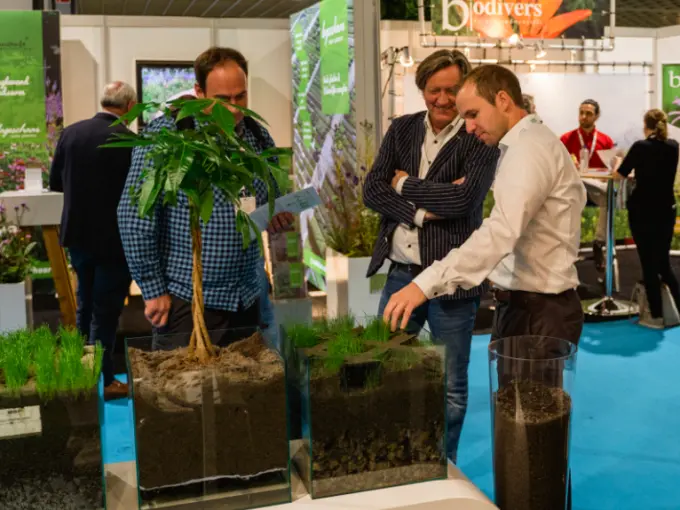 Bezoekers bekijken glazen bakken met bodemopbouw en een jong boompje