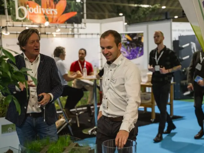Twee mannen in gesprek op een beursstand met bodemprofielen in glasbakken