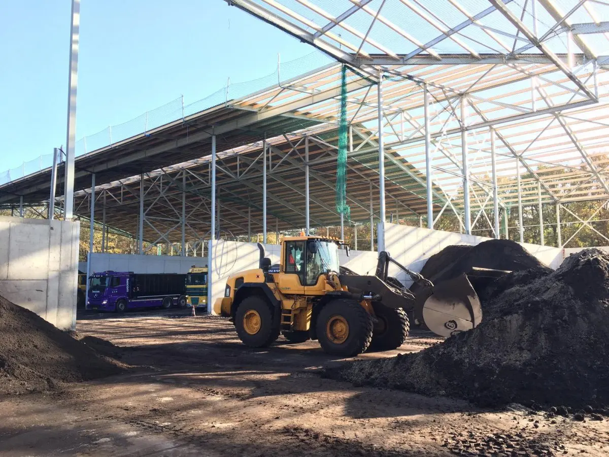 Gele shovel bij hopen zwarte grond onder een grote overkapping