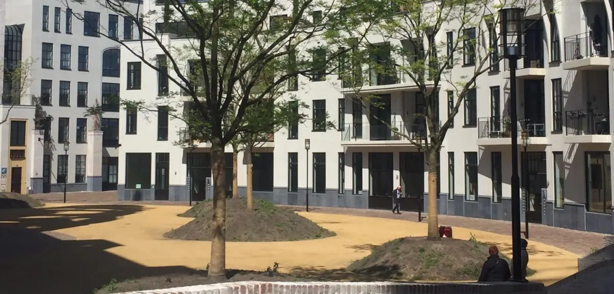Jonge bomen en grasheuvels op een plein voor witte appartementen