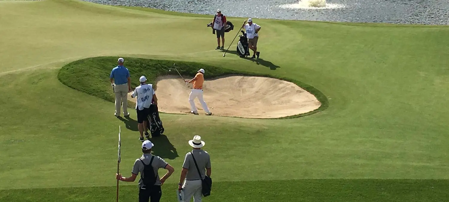 Golfer slaat de bal uit een zandbunker terwijl caddies toekijken