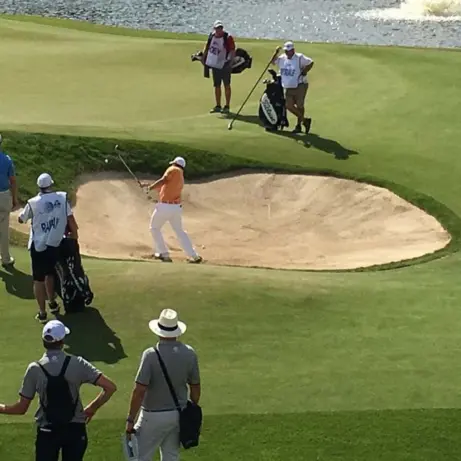 Golfer slaat de bal uit een zandbunker terwijl caddies toekijken