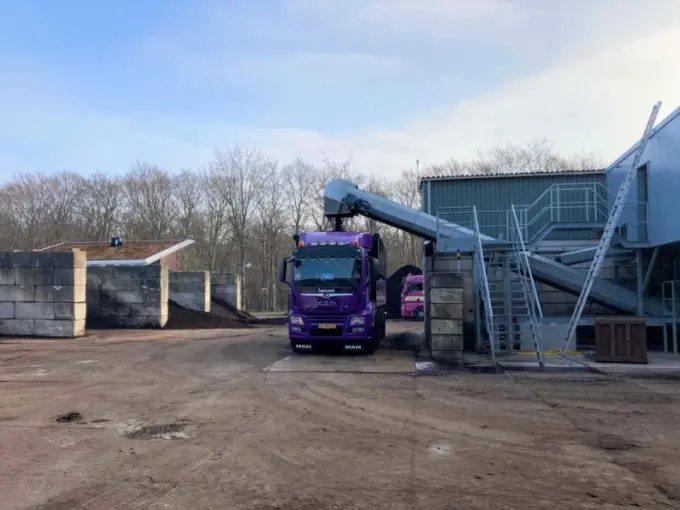 Paarse Heicom-vrachtwagen wordt met een transportband geladen op het bedrijfsterrein