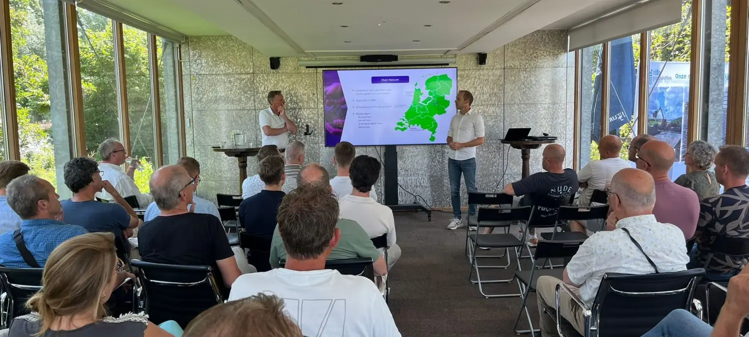 Publiek luistert naar twee sprekers bij een scherm met een Nederlandkaart