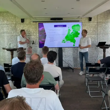 Publiek luistert naar twee sprekers bij een scherm met een Nederlandkaart