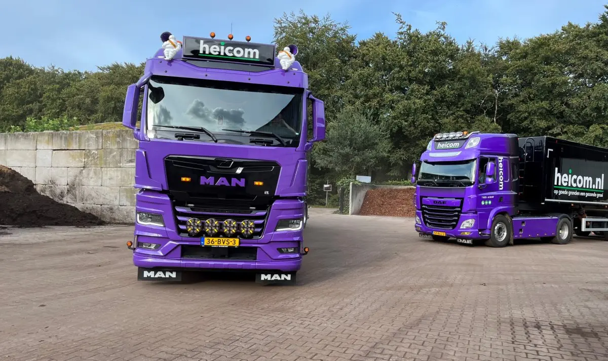 Twee paarse Heicom-trucks op klinkerverharding, een MAN vooraan en een DAF ernaast