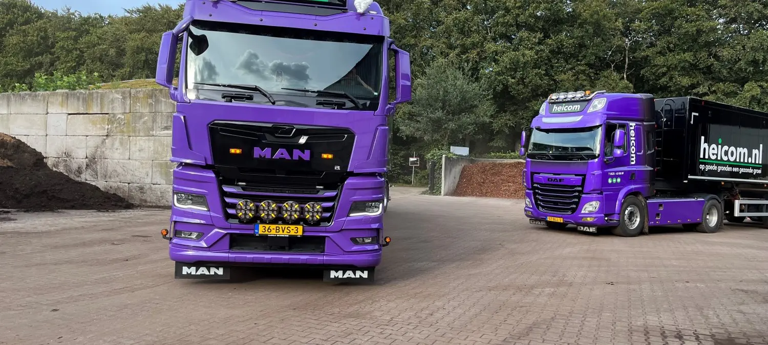 Twee paarse Heicom-vrachtwagens op een erf, vooraan een nieuwe MAN-trekker