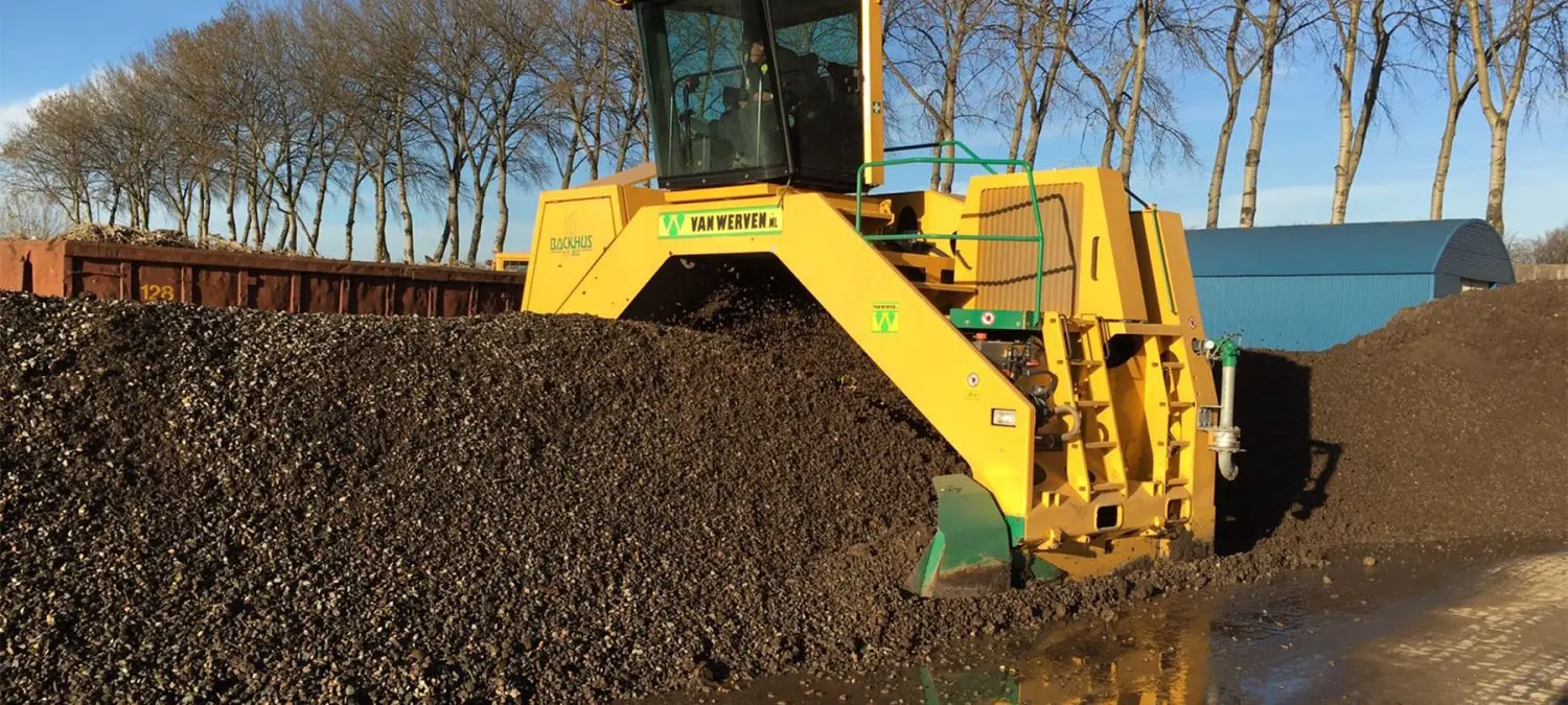 Gele compostkeerder keert een lange donkere composthoop om
