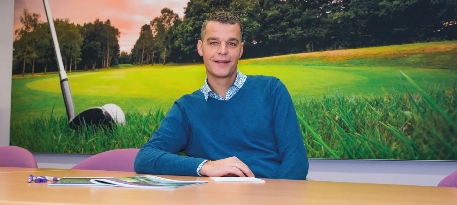 Man in blauwe trui aan tafel voor een wandfoto van een golfbaan