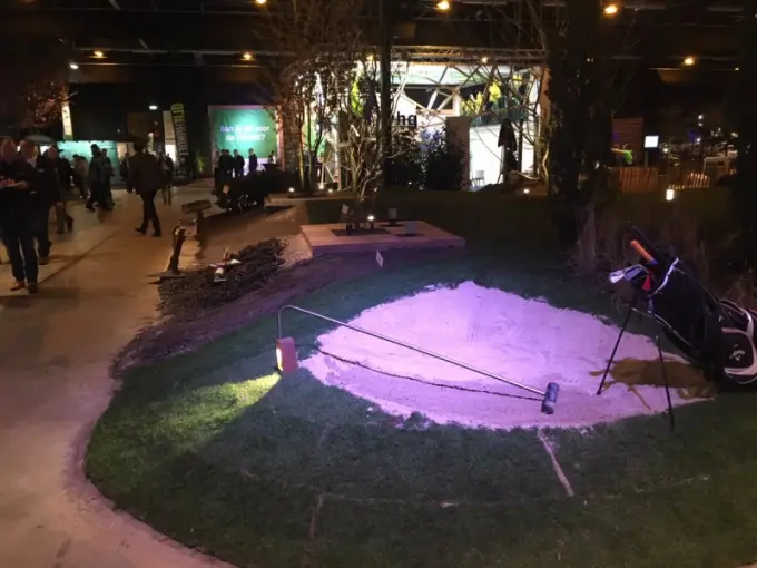 Nagebouwde golfbunker met wit zand en golftas in een beurshal
