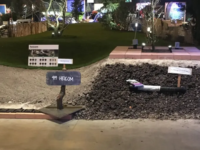 Beursvak met hopen zand en zwart granulaat en een bordje Heicom