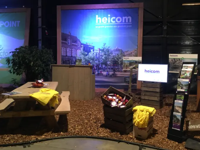 Beursstand van Heicom met picknicktafel, appelkisten en brochurerek op houtsnippers