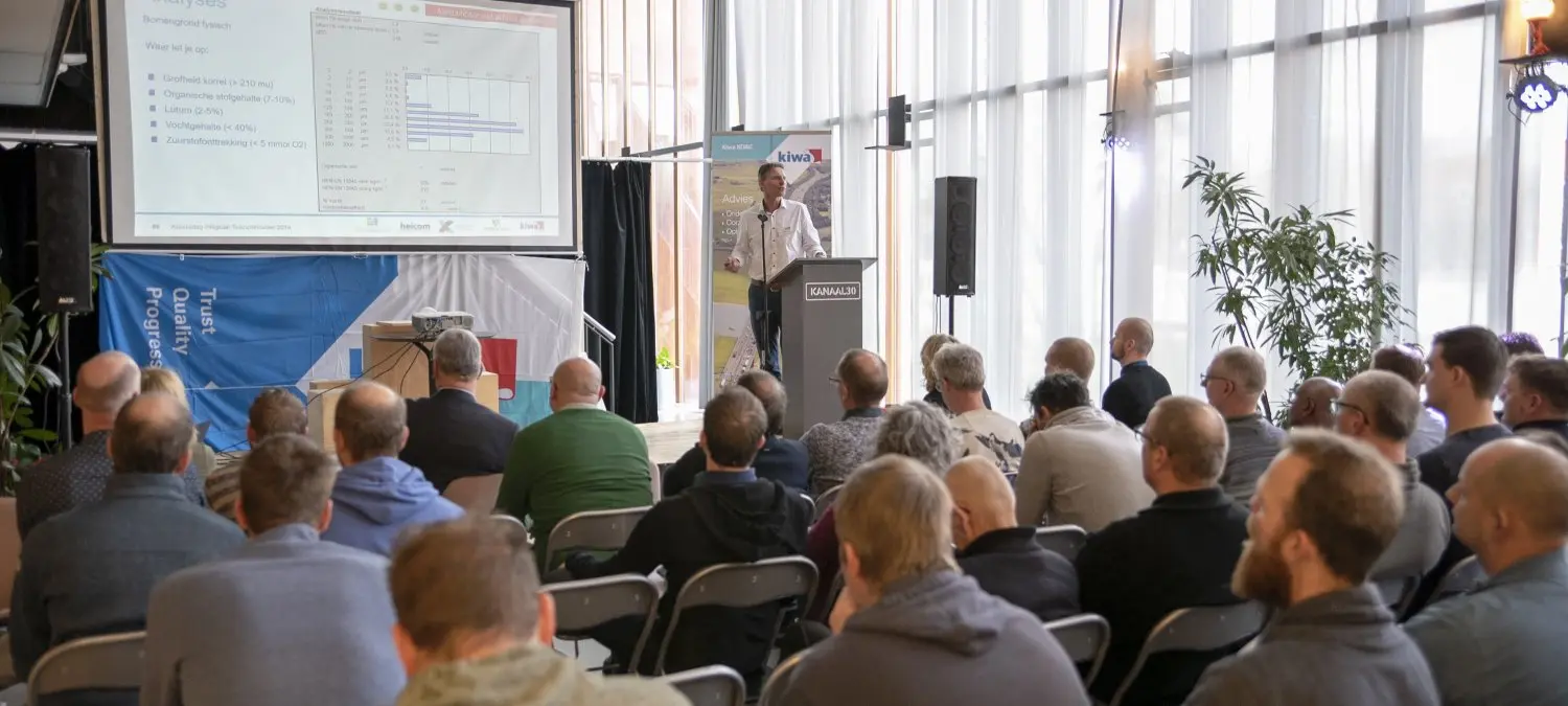 Spreker achter een katheder presenteert grafieken aan een zittend publiek