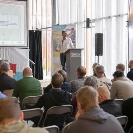 Spreker achter een katheder presenteert grafieken aan een zittend publiek
