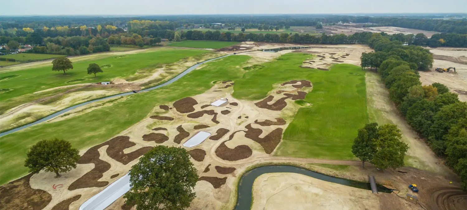 Luchtfoto van een golfbaan in aanleg met zandbunkers en een sloot