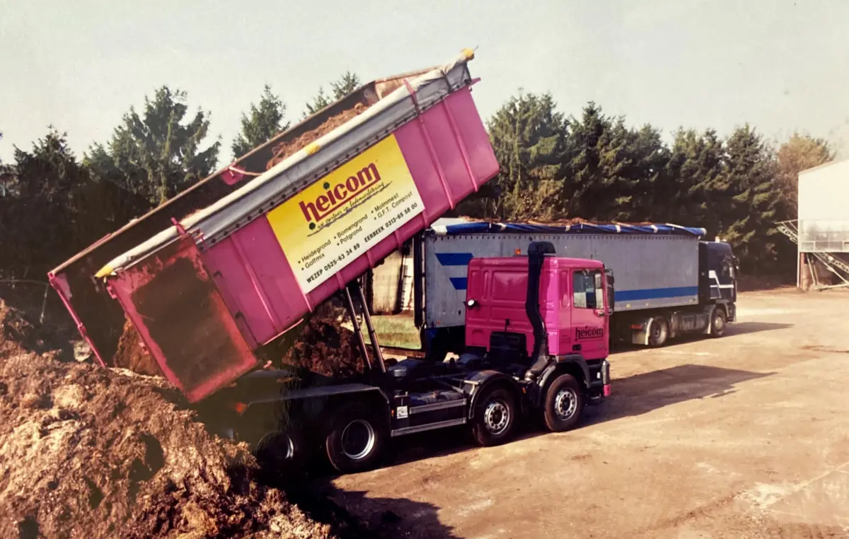 Roze Heicom-vrachtwagen kiept zijn container leeg naast een blauwe oplegger