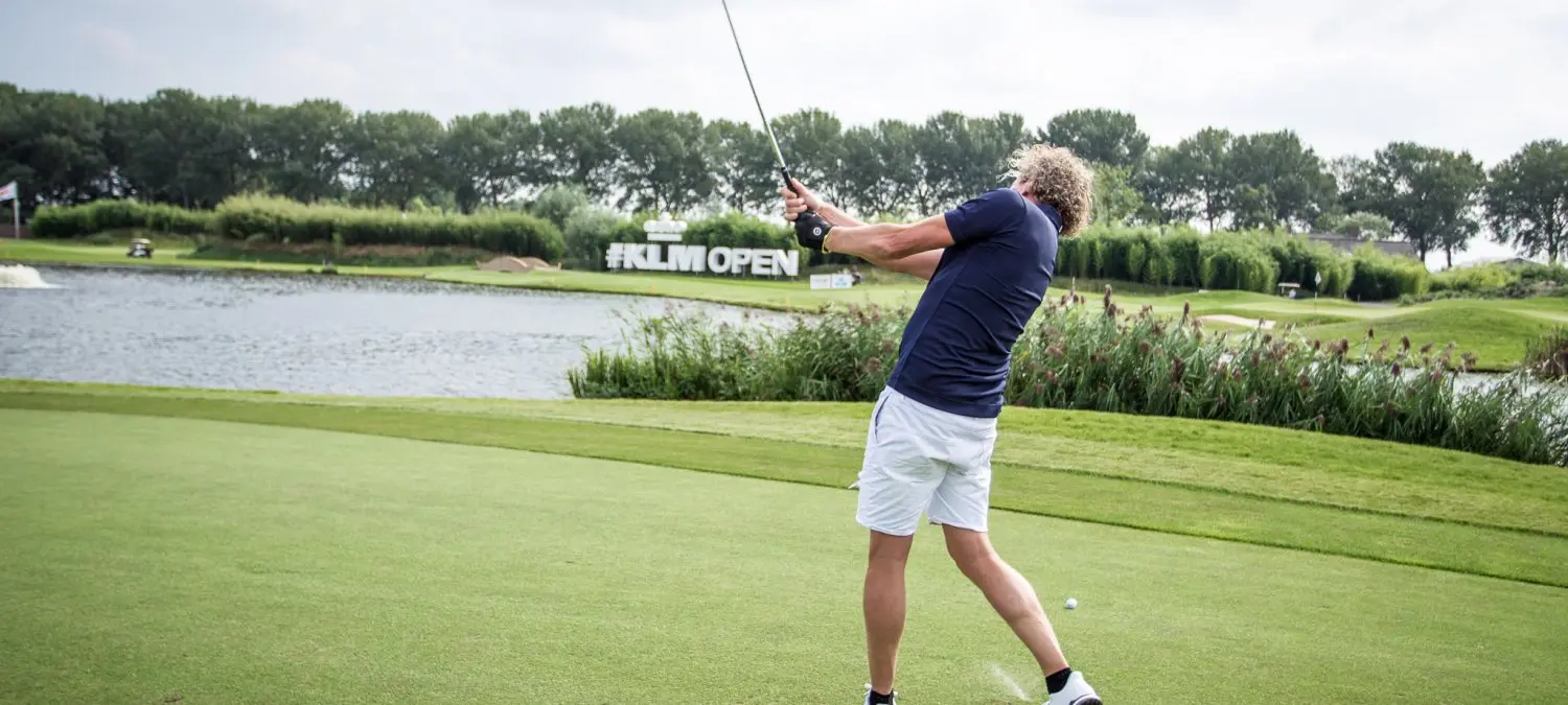 Golfer slaat af op een green langs water bij het KLM Open
