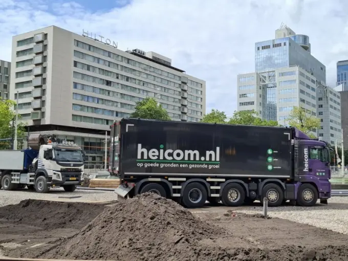 Vrachtwagen van Heicom naast grondhopen voor het Hilton-hotel in de stad