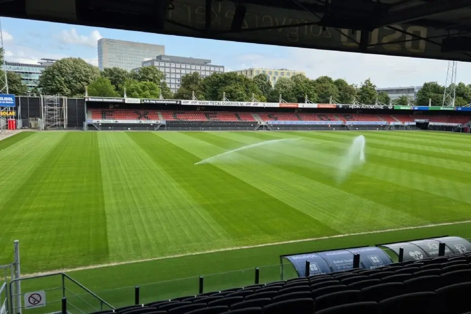 Beregening sproeit water over de grasmat, gezien vanaf de tribune