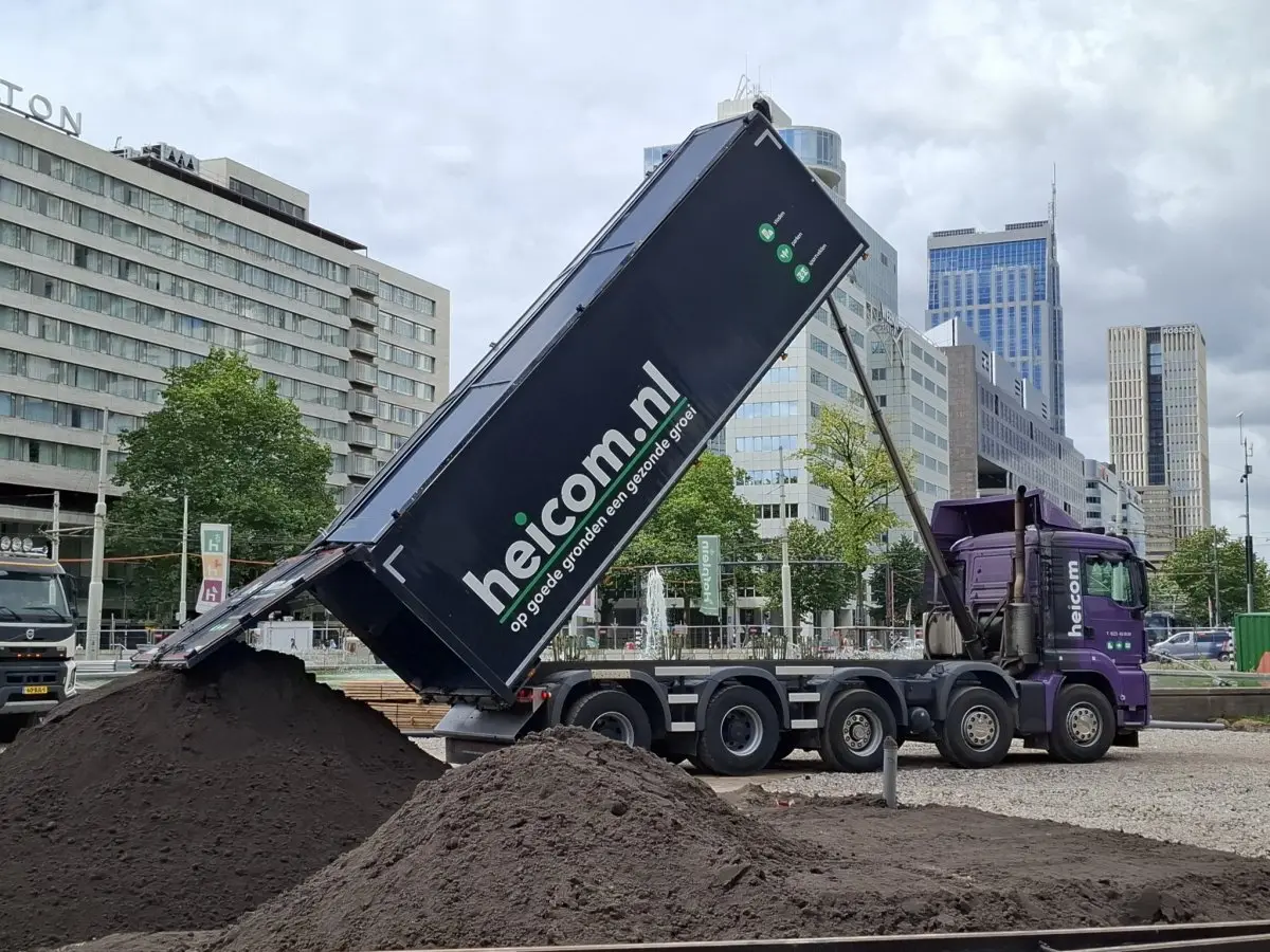 Kipper van Heicom stort donkere grond op een plein in de stad