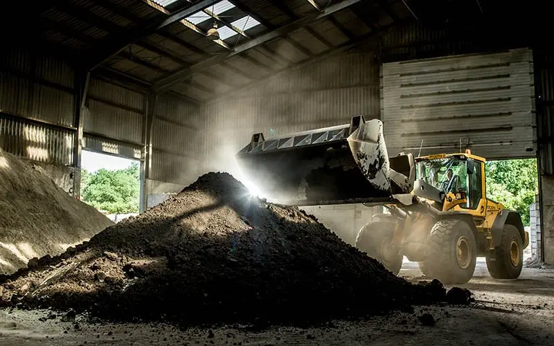 Shovel stort donkere grond op een hoge kegelvormige hoop in een loods