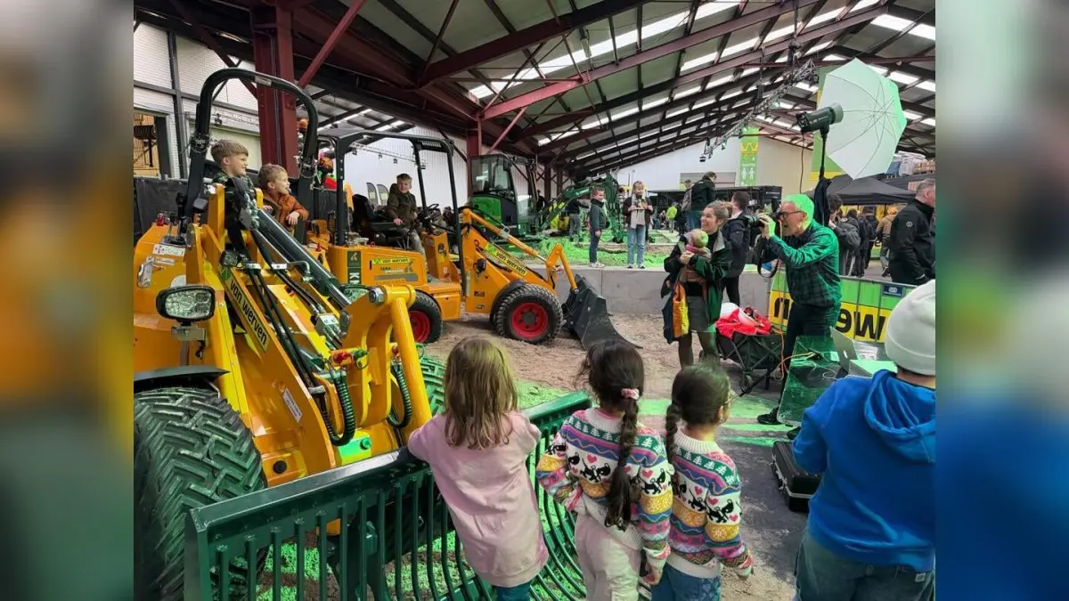 Kinderen kijken naar een gele shovel in een hal vol machines