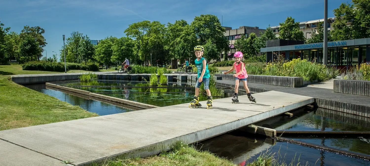 Twee kinderen skeeleren over een betonnen brug in een stadspark